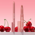 ColourPop Lippie Pencil "Oh Snap" stands uncapped with a creamy soft pink-nude tip, paired with matching Lippie Stix, on a countertop with glossy red cherries against a pink gradient backdrop - ideal for precise, long-wear lip lining.