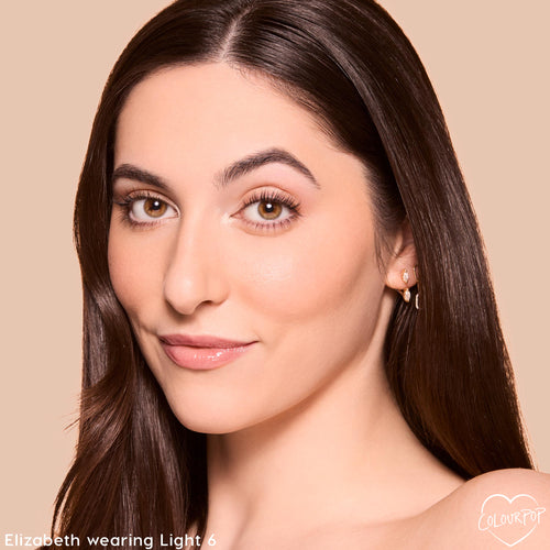 Close-up of a woman’s smooth, natural-looking face wearing Colourpop Pretty Fresh Tinted Foundation Balm in shade Light 6, showing even coverage and a soft glow against a beige background.