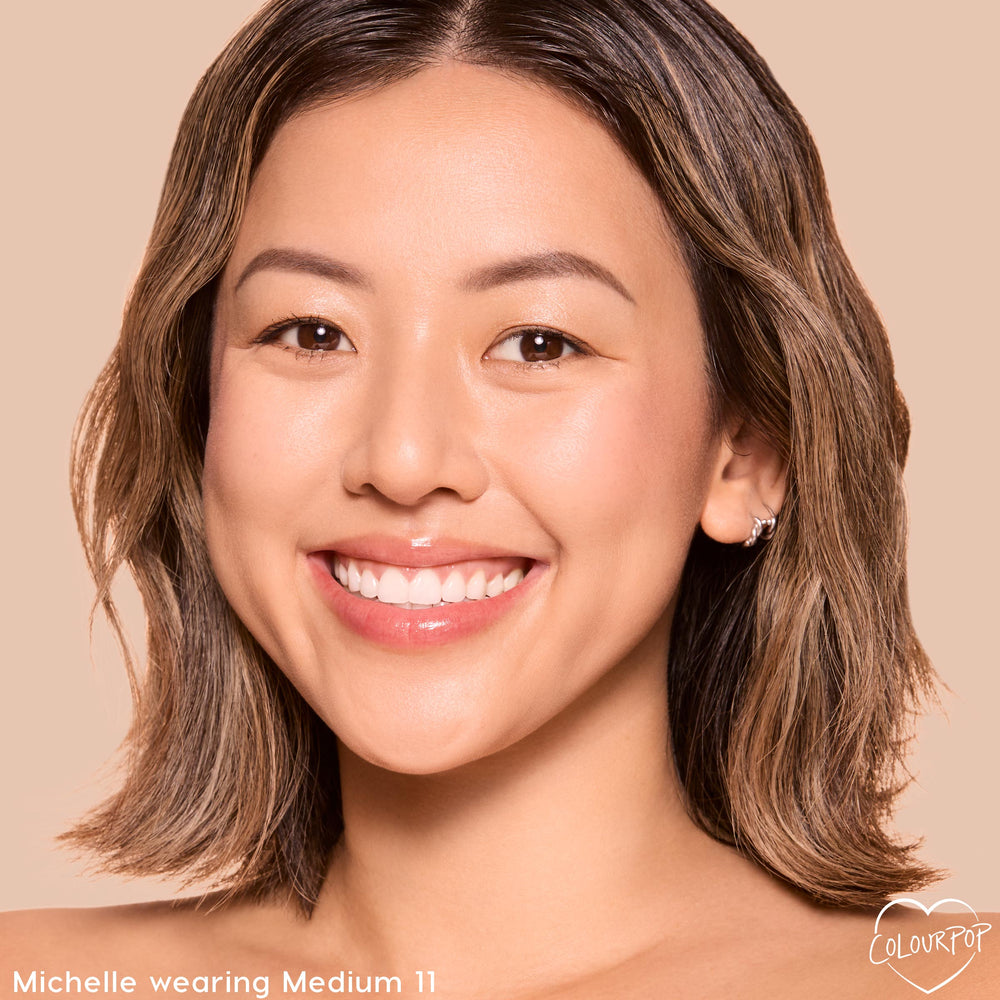Model smiling while wearing ColourPop Pretty Fresh Tinted Foundation Balm in Medium 11, showcasing smooth, natural dewy coverage on an even complexion; close-up face against a warm beige background to help shoppers gauge the Medium 11 shade.