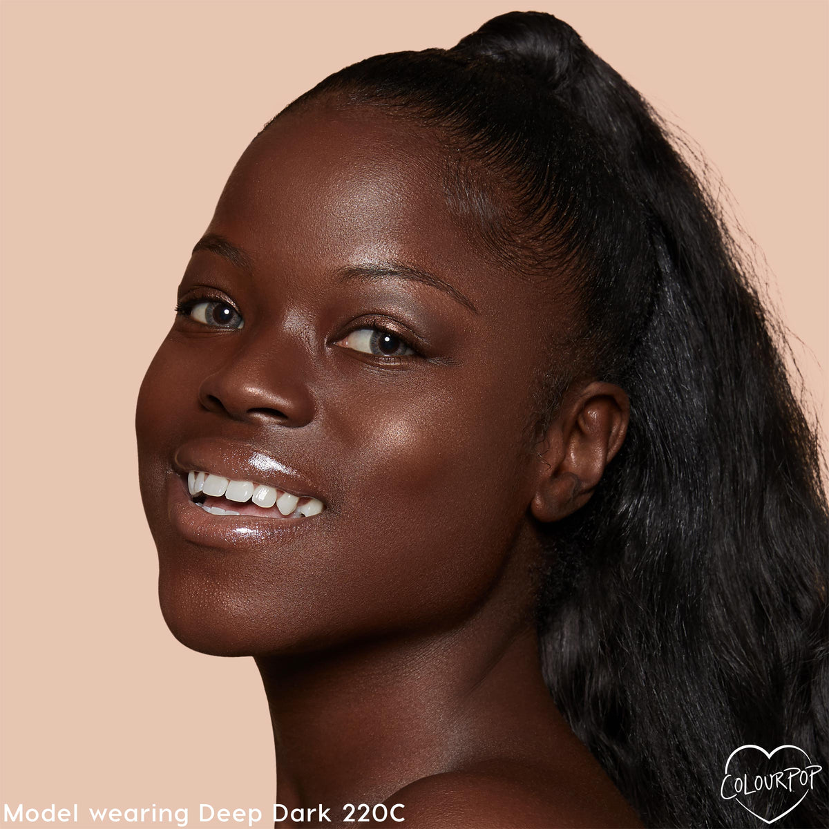 Smiling model showcases ColourPop Pretty Fresh Creamy Concealer in Deep Dark 220 C, revealing smooth, radiant, skin-like coverage; close-up studio portrait with glossy lips, high ponytail, and peach background with ColourPop logo.