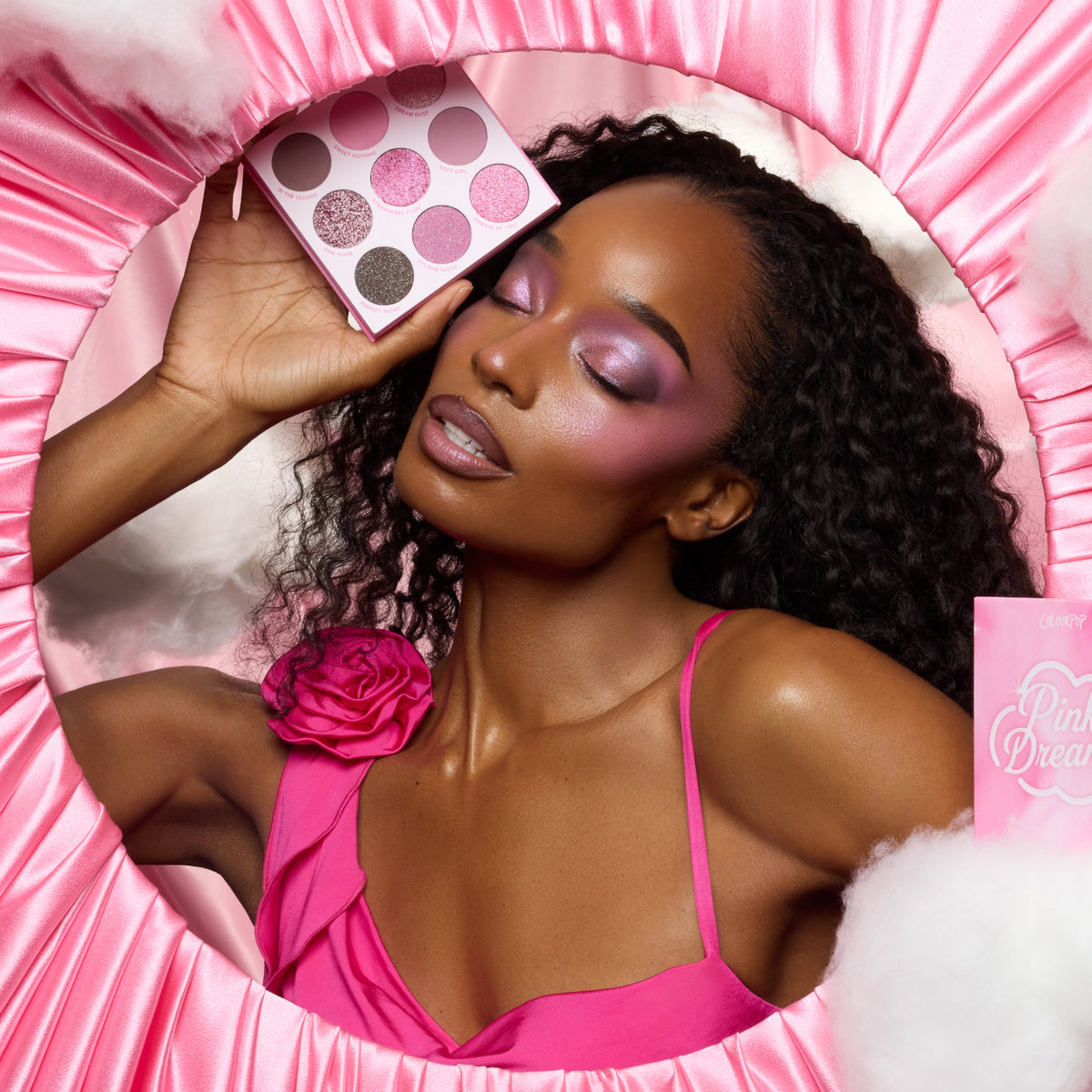 Model with deep skin holding the Pink Dreams palette, wearing pink shimmer shadow in a pink satin frame