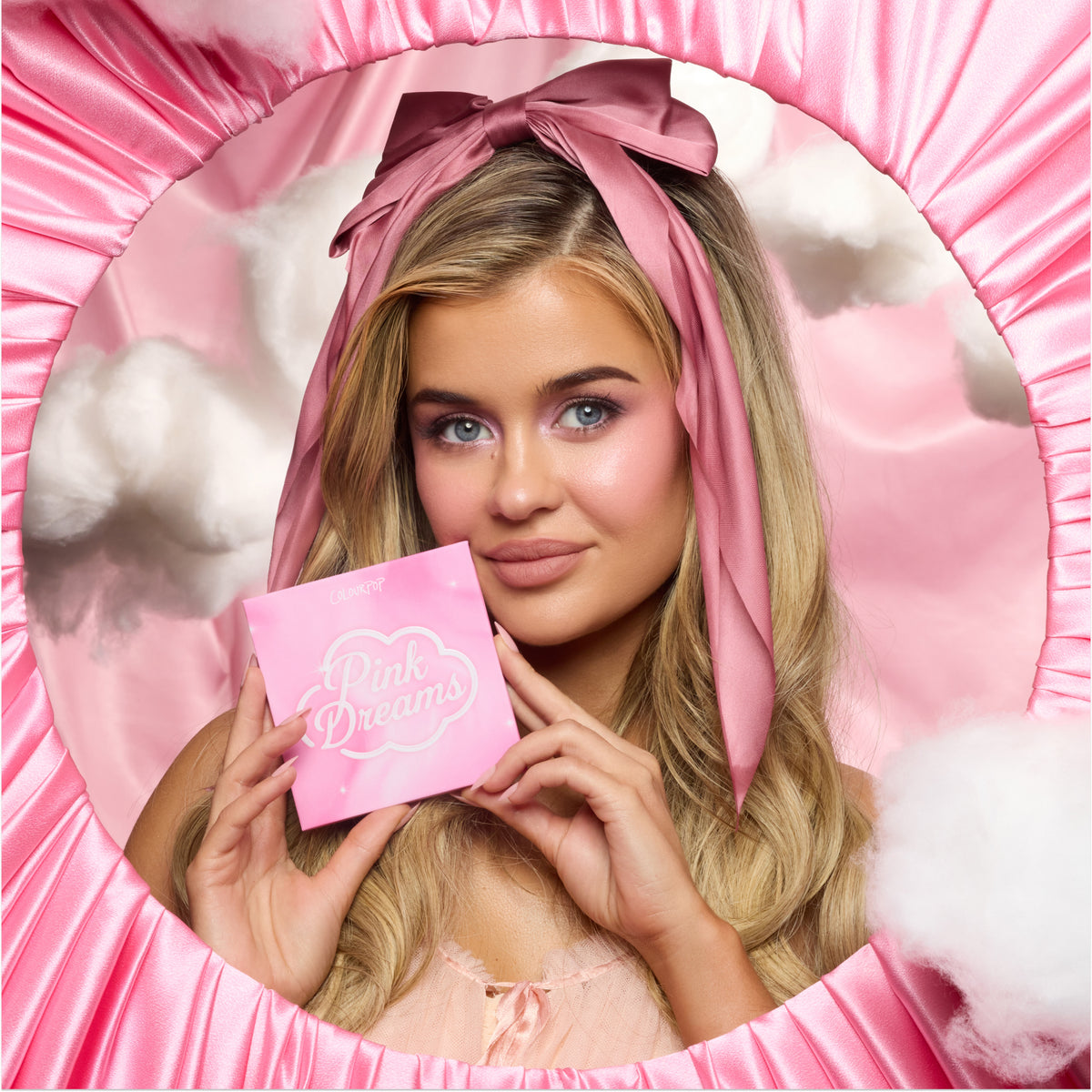 Model with fair skin and a pink headscarf holding the Pink Dreams palette in a pink satin frame