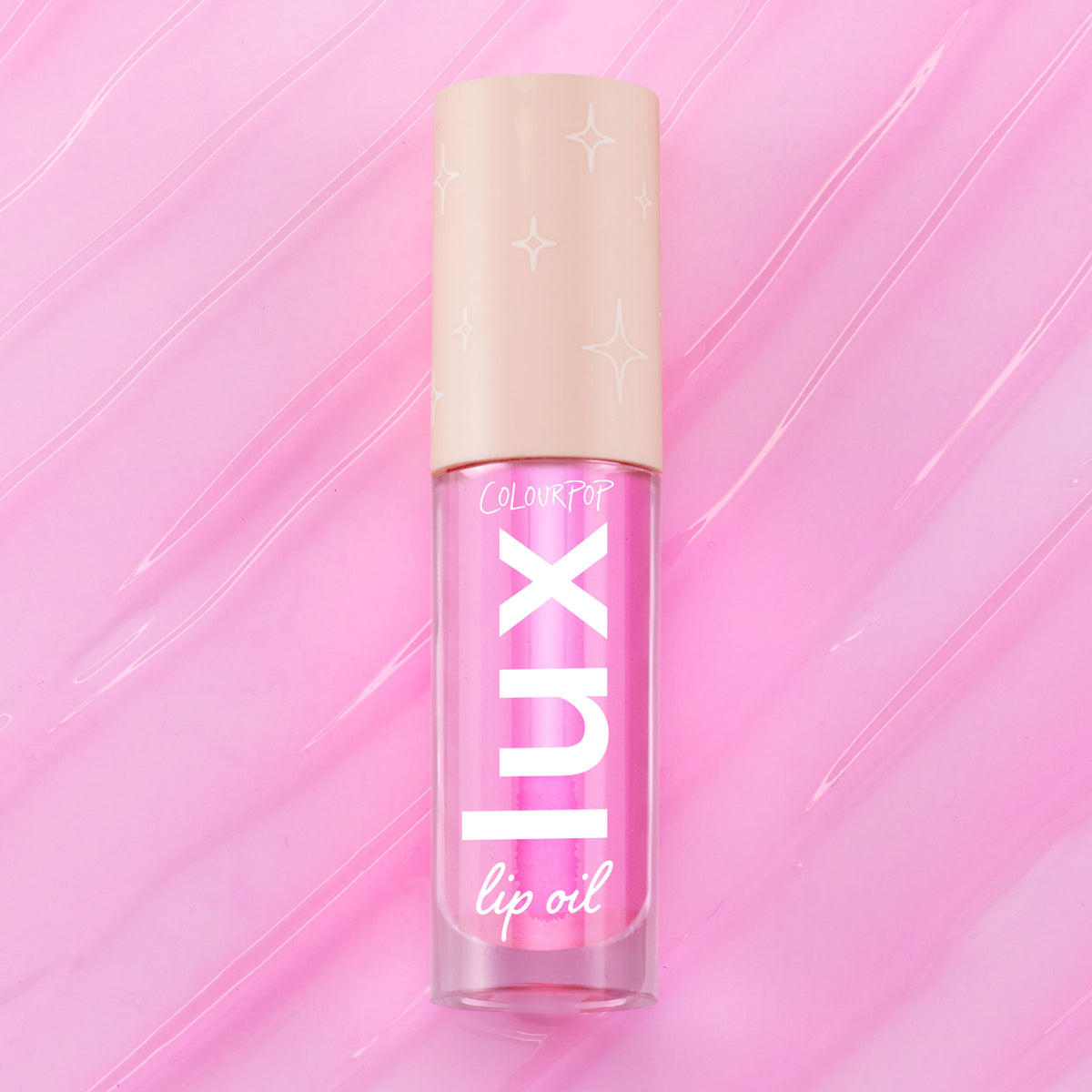 ColourPop Lux Lip Oil in Raspberry Mojito, a clear tube with bold “LUX” lettering and a beige star-print cap, displayed on a glossy swirled pink background, showcasing the vibrant pink-tinted lip oil formula.
