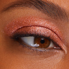 Shimmering copper eyeshadow coats a brown eye, showcasing Flamethrower, a metallic shade of ColourPop Super Shock Shadow, with glittery payoff swept across the lid and crease, accenting soft lashes and skin texture in a tight beauty close-up.