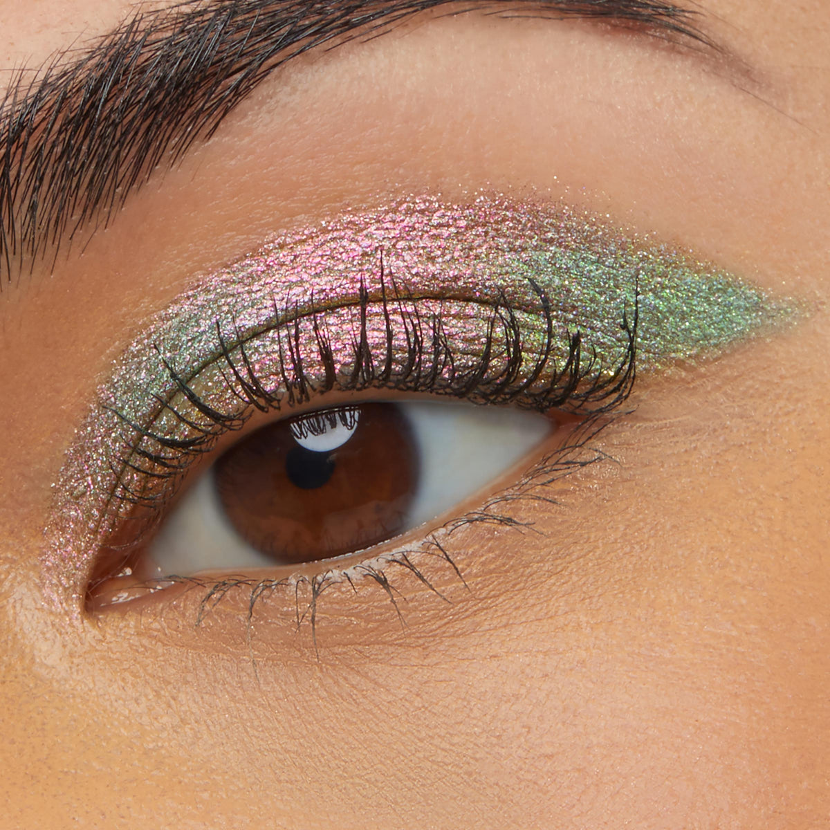 Close-up of a brown eye wearing Colourpop Galaxy Shadow Stix, showing a smooth swipe of metallic duochrome pink-to-green shimmer eyeshadow across the lid for a bold, iridescent makeup look.