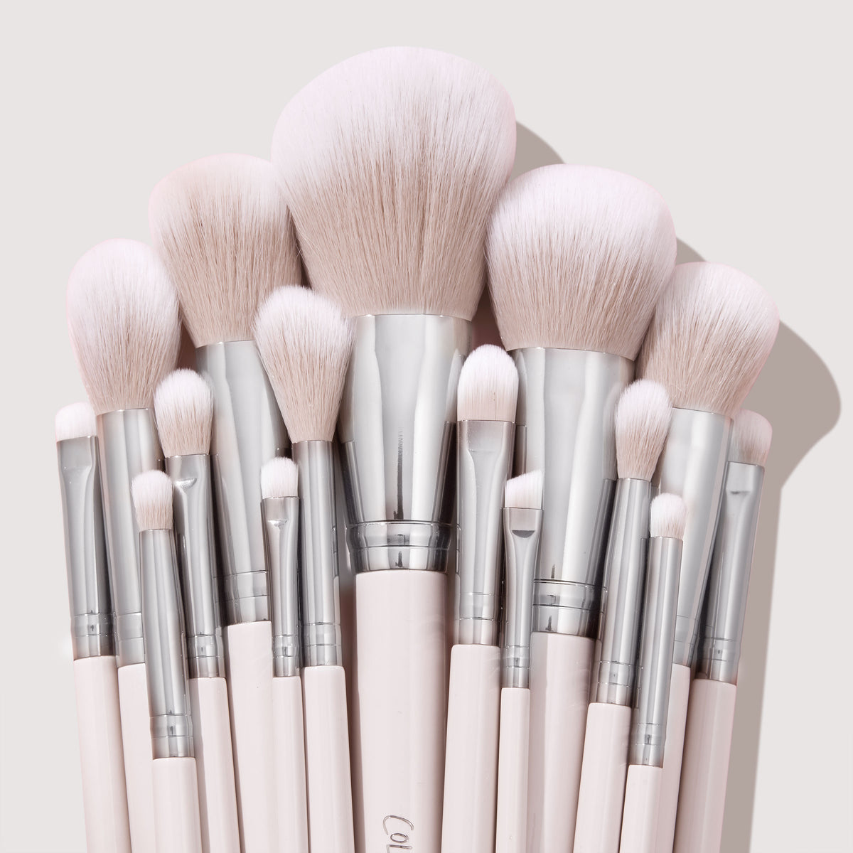 Metallic Mood brushes fan out in a tight cluster, showcasing soft blush-pink bristles, chrome ferrules, and pale pink handles on a light backdrop - part of the ColourPop Shadow Palette & Brush Set for precise eye and face makeup.