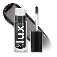 Team Jacob ColourPop Lux Lip Oil displayed open, doe-foot applicator beside the tube and a glossy charcoal-black swatch with silver shimmer behind, highlighting the sheer, high-shine finish; cap off on a white studio backdrop.