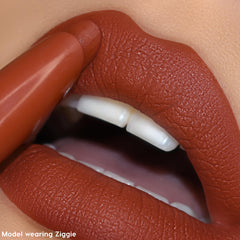 Ziggie ColourPop Lippie Stix coats lips as the bullet applies a warm terracotta brown, creating a soft-matte, full-coverage finish in a tight close-up, highlighting smooth texture and a precise lip line.