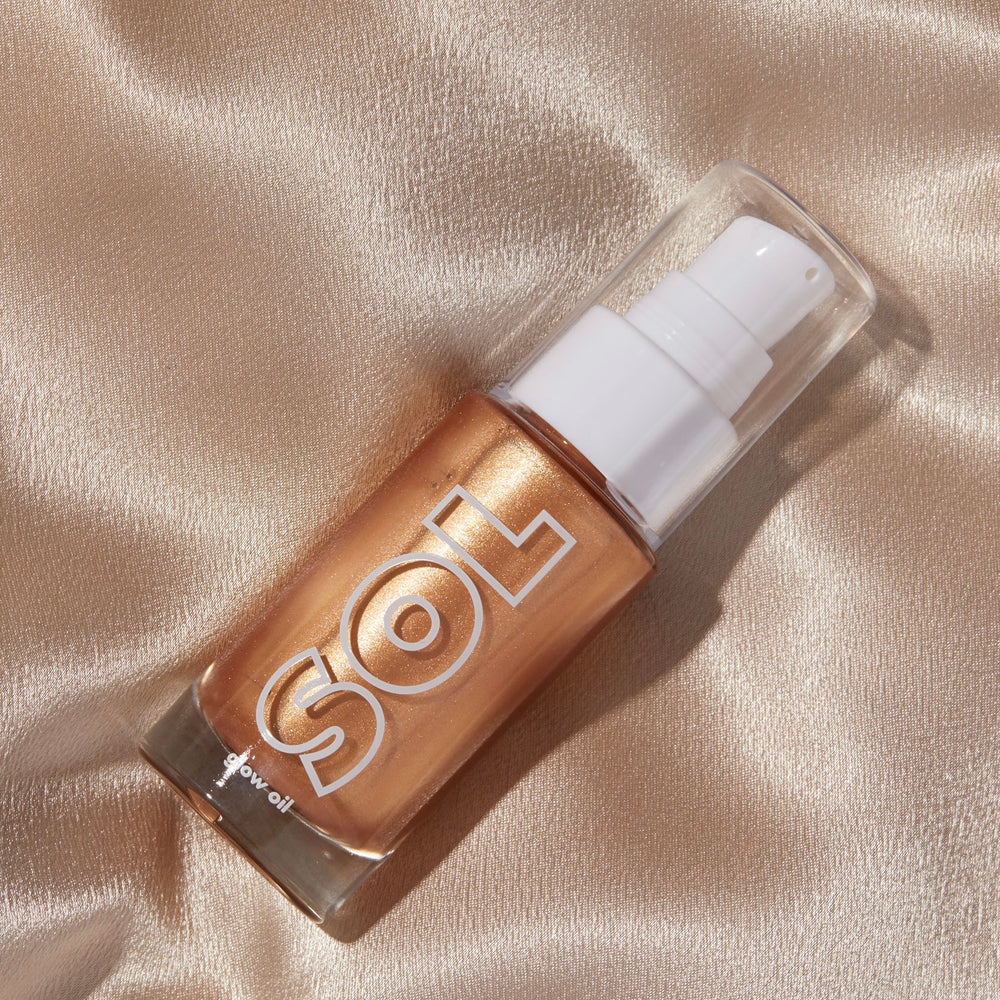 ColourPop SOL Glow Oil in shade Golden rests angled on champagne satin, a clear pump‑topped glass bottle with bold SOL logo, its bronze‑gold shimmer catching the light for a sun‑kissed body glow.