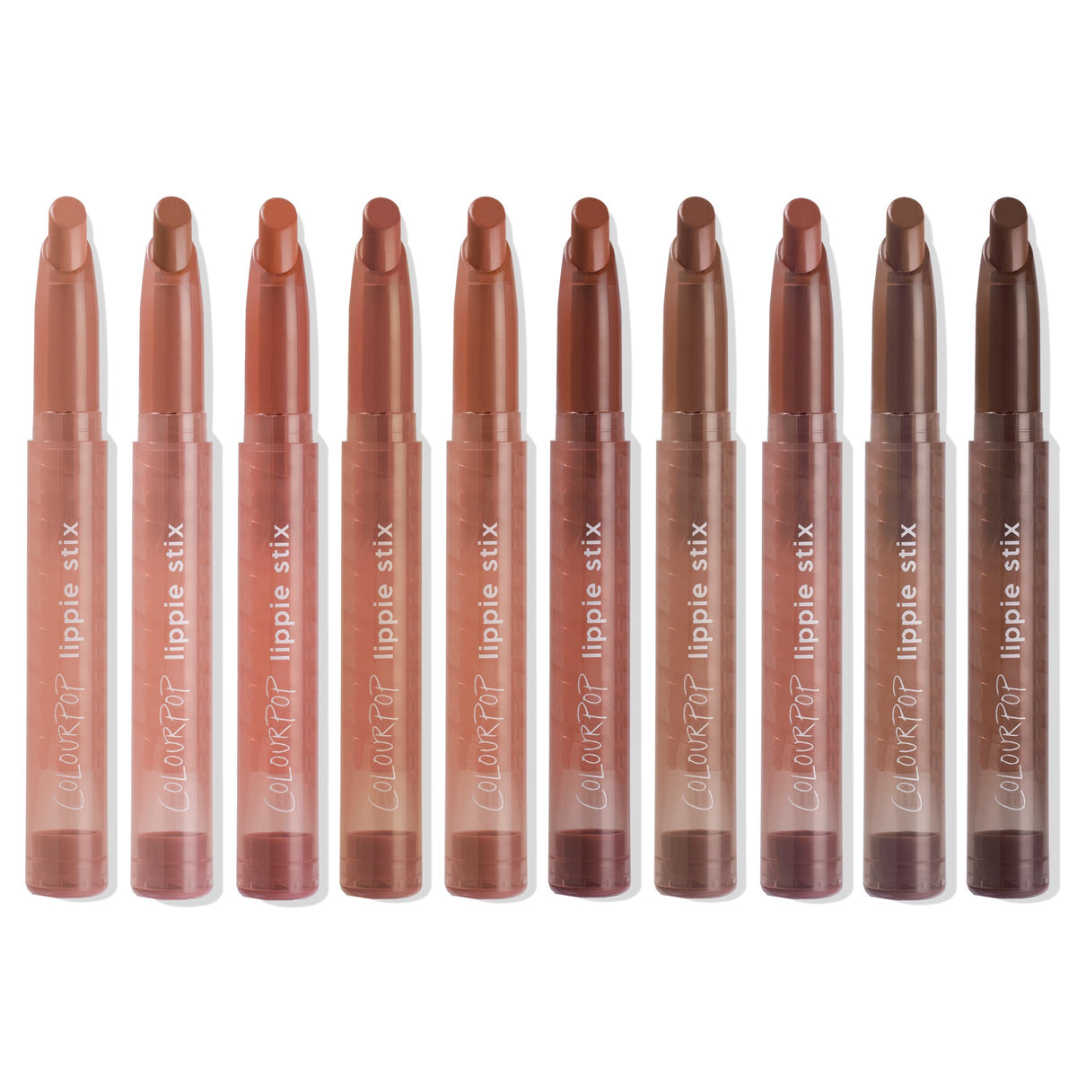 ColourPop Lippie Stix line up showing In the Nude collection - ten twist-up lipsticks in clear tubes, ranging from peach and pinky beige to warm caramel and deep brown - standing upright on a white background.