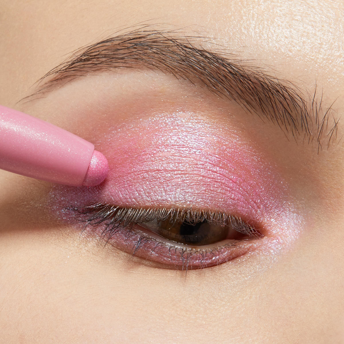 Juicy Gossip ColourPop Shadow Stix gliding over the eyelid, depositing shimmery bubblegum-pink color with a pearly finish; a tight eye close-up with natural brow showcases the creamy, blendable payoff.