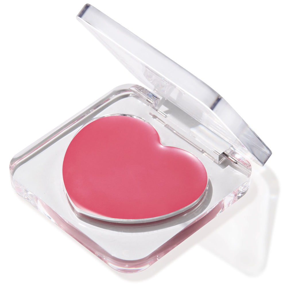 Heart-shaped pink balm in the Verified shade sits in a half-open clear compact, glossy pan catching light on a white background; multitasking ColourPop Lip and Cheek Balm for buildable tint on lips and cheeks.