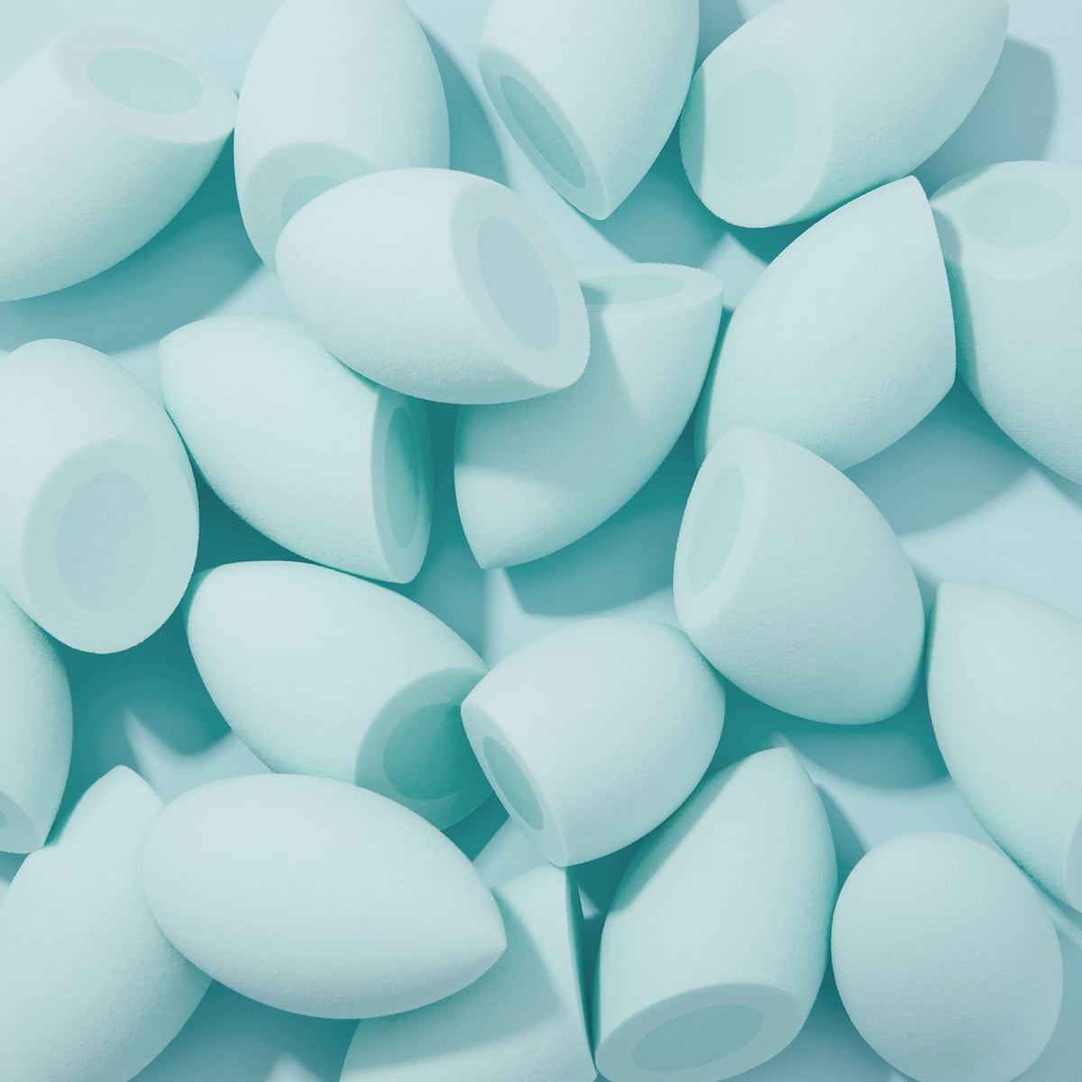 Silicone Blending Sponge blending foundation - multiple mint teardrop sponges with flat bases scattered on a pale aqua surface, ready for precise makeup application; essential ColourPop Makeup Tools & Accessories for smooth, streak-free coverage.