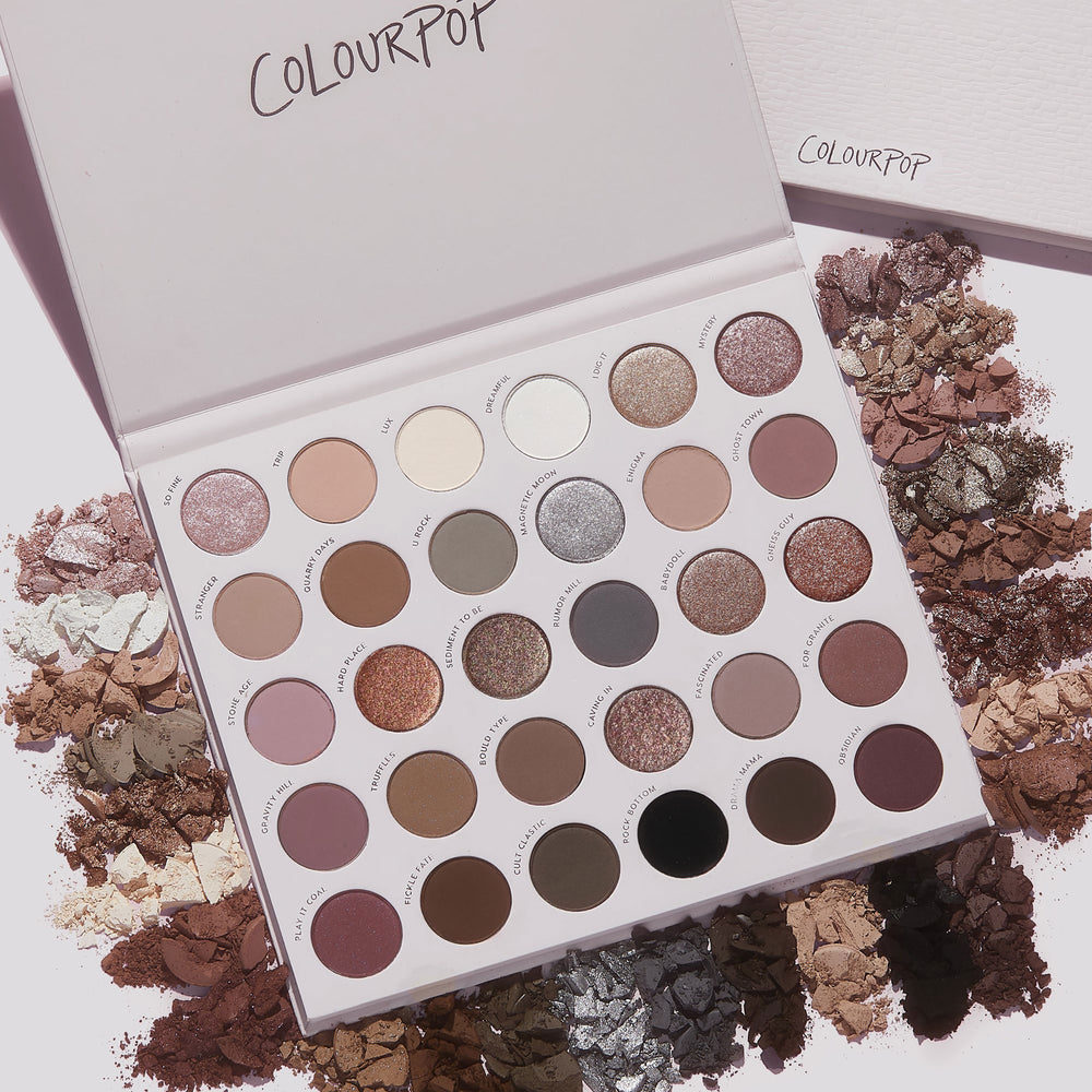 Stone Cold Fox ColourPop Shadow Palette lying open, displaying 30 cool‑toned neutral eyeshadows in matte and shimmer finishes; taupe, mauve, gray and champagne pans ringed by crushed powder swatches on a light backdrop.