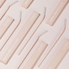 ColourPop Brow Brush with soft pink handle and clear spoolie head, arranged diagonally on a pale pink backdrop beside matching feather effect brow brush boxes, showcasing a makeup brush for shaping and feathering eyebrows.