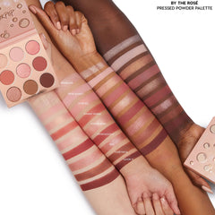 By The Rosé 9-pan pressed‑powder ColourPop Shadow Palette shown open with rose, mauve, and bronze mattes and shimmers, with swatches across three arms in light, medium, and deep skin tones to show payoff; blush‑pink packaging on white.