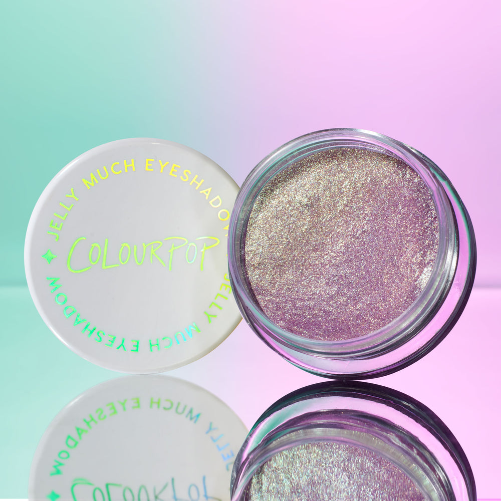 Open jar of ColourPop Jelly Much Shadow in Big Ego showcasing a shimmering lavender-silver gel eyeshadow, set beside its white lid with iridescent logo on a pastel mint-and-pink gradient surface with a mirrored reflection.