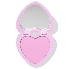 Cupid’s Bow ColourPop Pressed Powder Blush sits open, showcasing a baby‑pink heart‑shaped pan and built‑in mirror in a pastel lavender heart compact on a white backdrop.