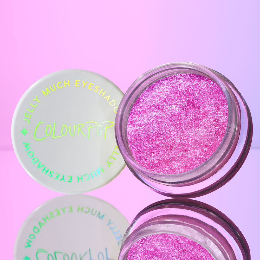 ColourPop Jelly Much Shadow in No Rest For The Vivid shown open, revealing vibrant hot-pink, metallic gel eyeshadow; white lid with holographic logo beside it on a mirrored surface against a pink–purple gradient background.