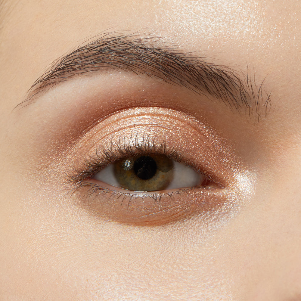 Eyelid wearing Honey BB ColourPop Shadow Stix, a warm honey‑gold shimmer cream eyeshadow, swept across the lid and inner corner for a glossy metallic glow, softly blended at the crease beneath a natural brow.